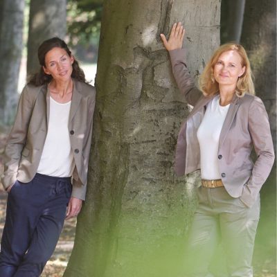 frauen-in-fuehrungspositionen_teamfuehrung_weibliche-fuehrung Frauen in Führungspositionen, Teamführung, 2 Frauen an einen Baum gelehnt