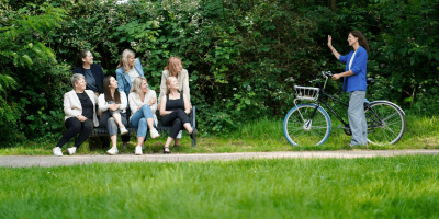Frauen in Führungspositionen, Female Leadership, Frauengruppe auf Bank und Frau mit Fahrrad kommt hinzu