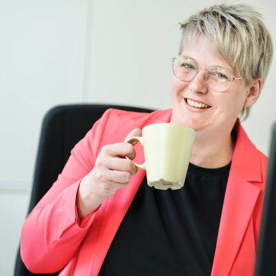 Gesund Arbeiten, psychologische Sicherheit, lachende Frau im roten Blazer hält eine Kaffeetasse